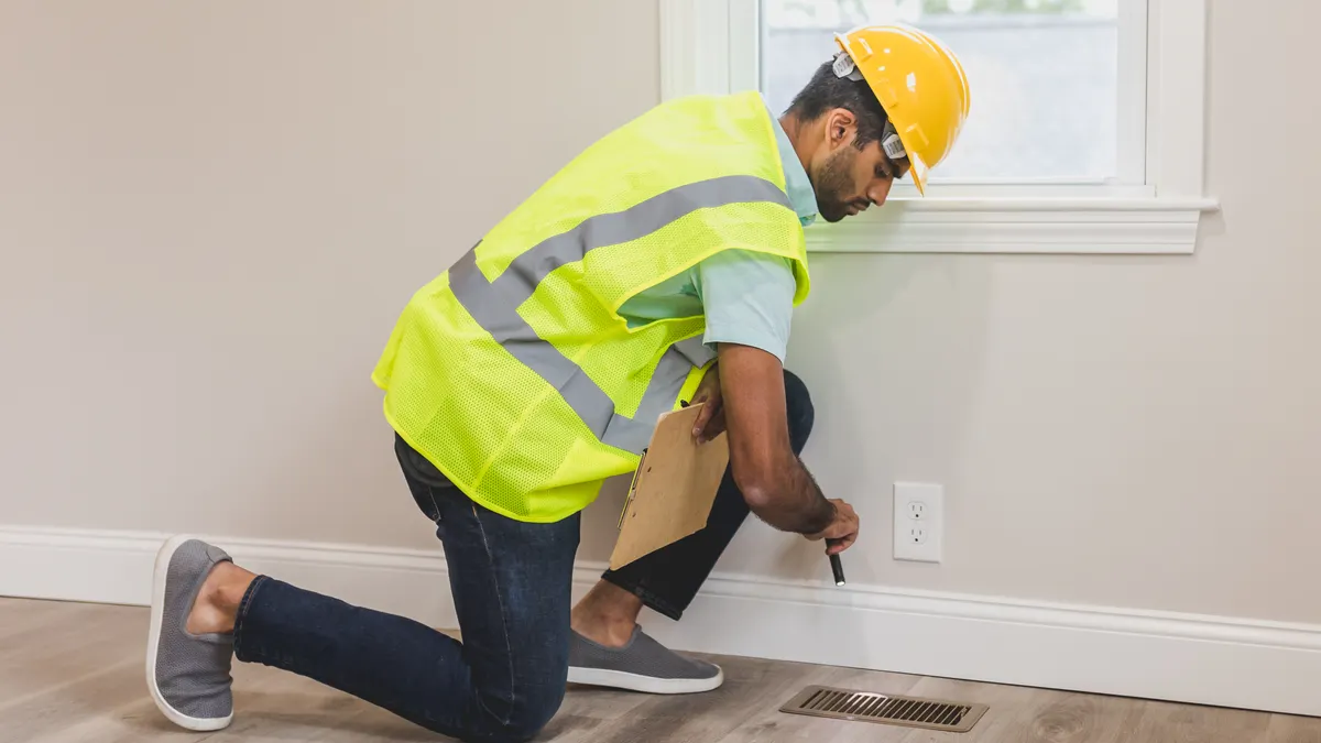 How to choose the right HVAC system size for your home HVAC technician checking a floor vent by the wall